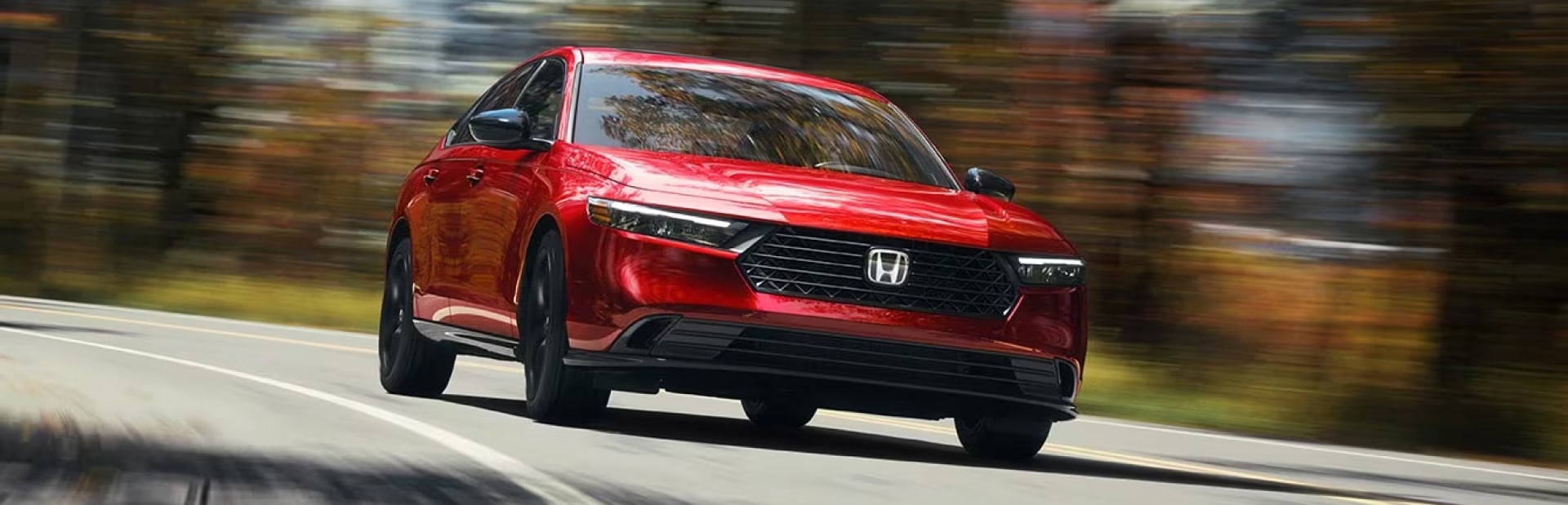 A red Honda accord hybrid driving down a road in autumn.